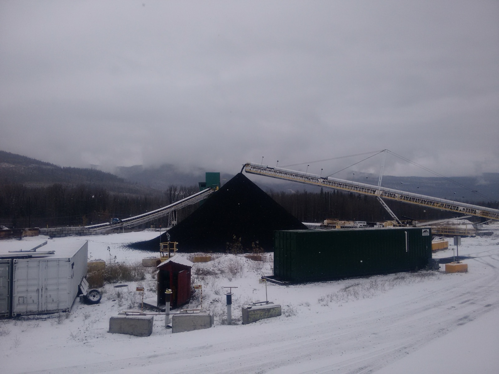 Snow-covered coal stockpile with conveyor belts and shipping containers