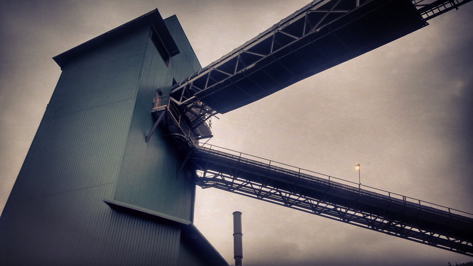 Underside of industrial conveyor bridges against an evening sky