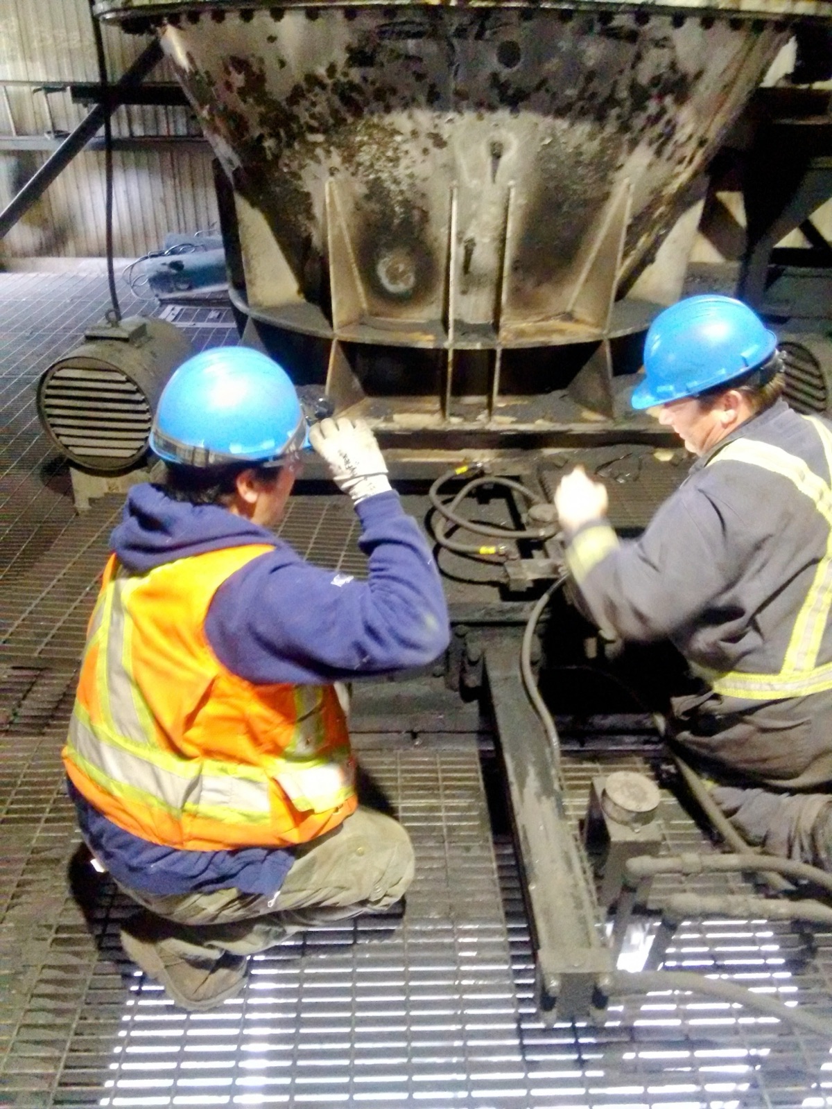 Two workers in personal protective equipment servicing industrial equipment